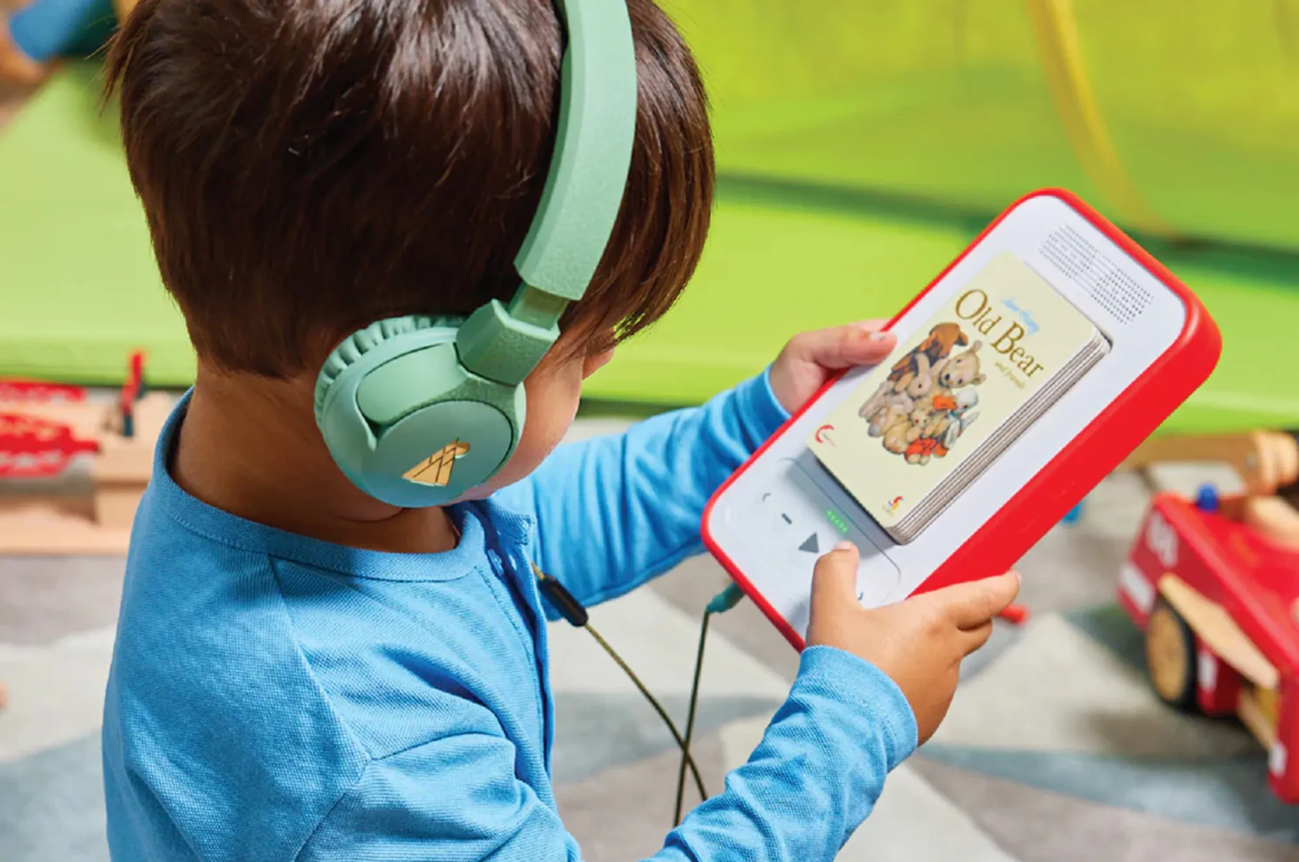 A child wearing headphones, holding the Voxblock audiobook player and looking at its screen.